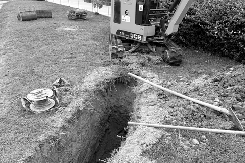Miniescavatore che apre uno scavo stretto in un giardino per la posa di una tubazione
